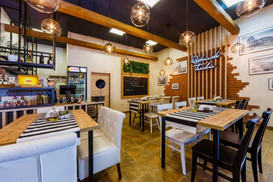 Sala restauracji z drewnianymi stołami, bieżnikami w pasy i szklanymi lampami