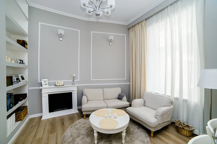 Salon w stylu klasycznym ze sztukaterią, kominkiem, jasną sofą i fotelem