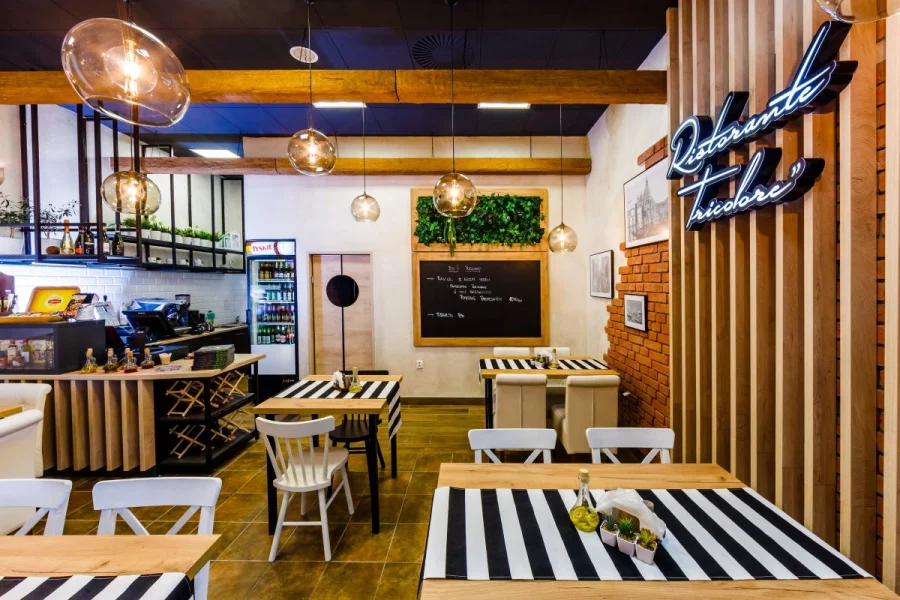 Restauracja z lamelami na ścianie, neonem i stołami z bieżnikami w czarno-białe pasy