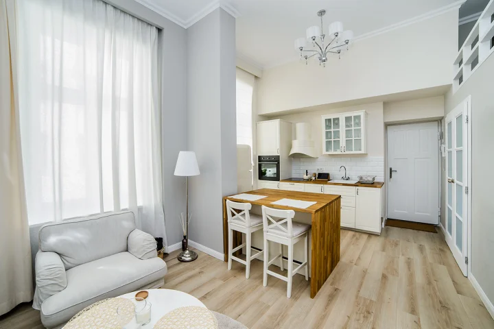 Salon z jasną sofą i stolikiem, w tle kuchnia z wyspą