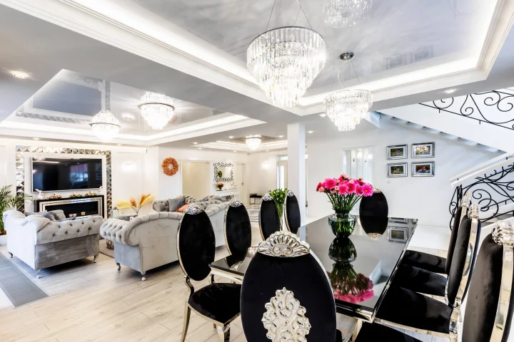 Salon z jadalnią w stylu glamour: czarne krzesła, kryształowe żyrandole i kominek