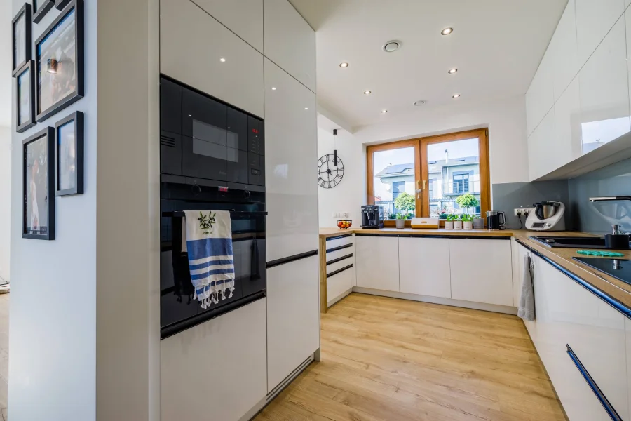 Kuchnia z białymi frontami na wysoki połysk, dębowym blatem i czarnymi uchwytami
