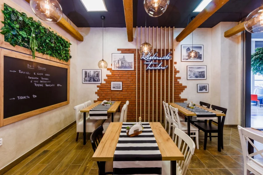 Stoliki przy ścianie z cegły, kredowa tablica z menu i drewniane lamele