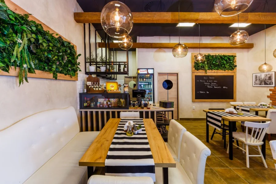 Restauracja z białą tapicerowaną ławką, zielonym panelem z roślin i drewnianymi belkami